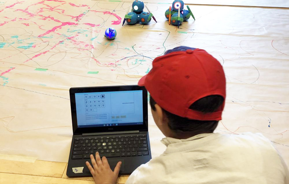 Student using early prototypes of Weavly with basic functionality to control robots and draw shapes with them. Student using Weavly simple prototype to build a program to direct robots on the floor.